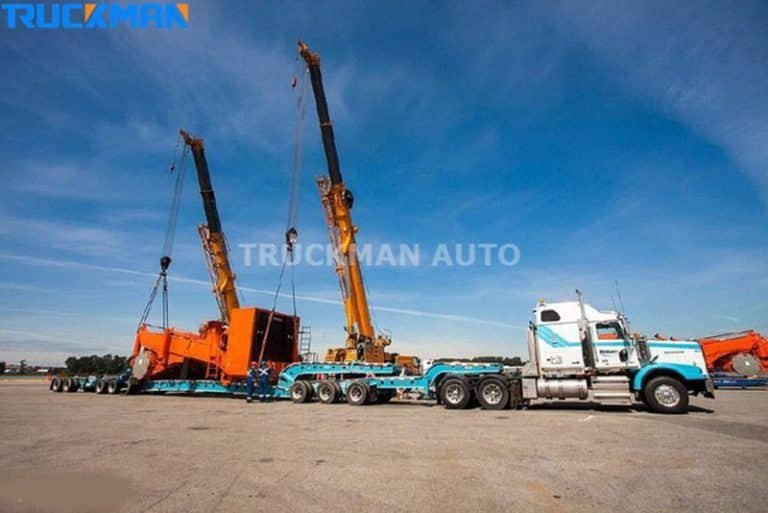 Two mobile cranes lifting heavy equipment onto a low-bed semi-trailer