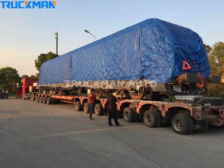 Oversized industrial machinery covered with a blue tarp on a low bed semi-trailer
