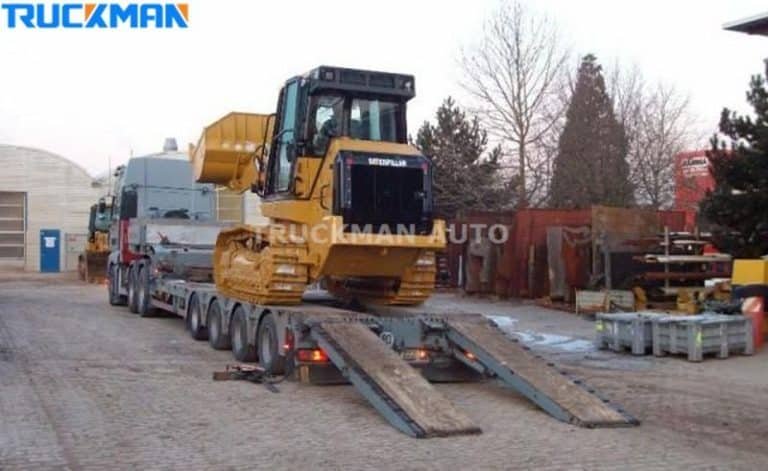 Caterpillar construction machinery being loaded onto a low-bed semi-trailer with metal ramps