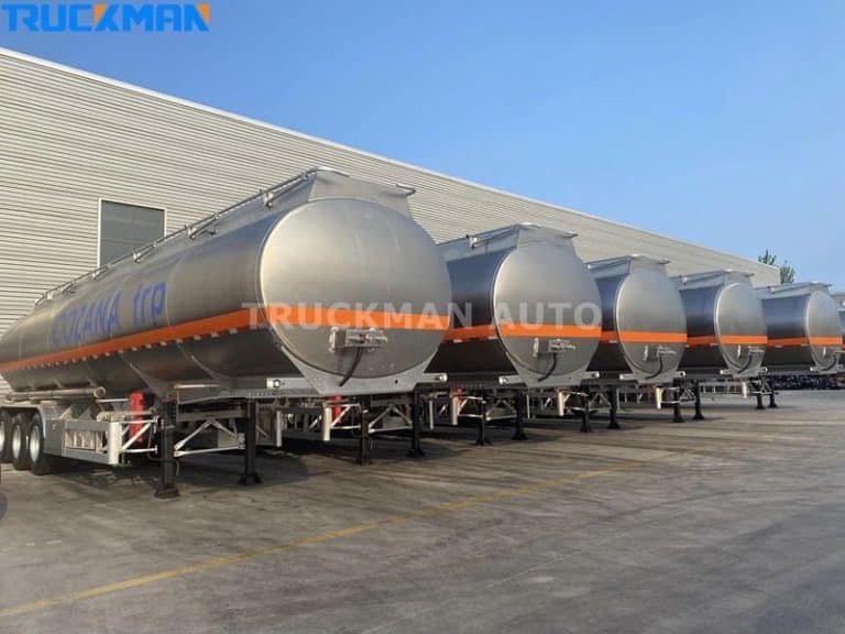 A train of silver-coloured fuel-burning tankers with 'COZAMA GROUP' branding parked in front of a warehouse