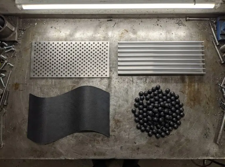 Four fuel tanker trailer baffle types on a workbench — fixed transverse plate, longitudinal fin baffle, flexible composite panel, and rubber baffle balls